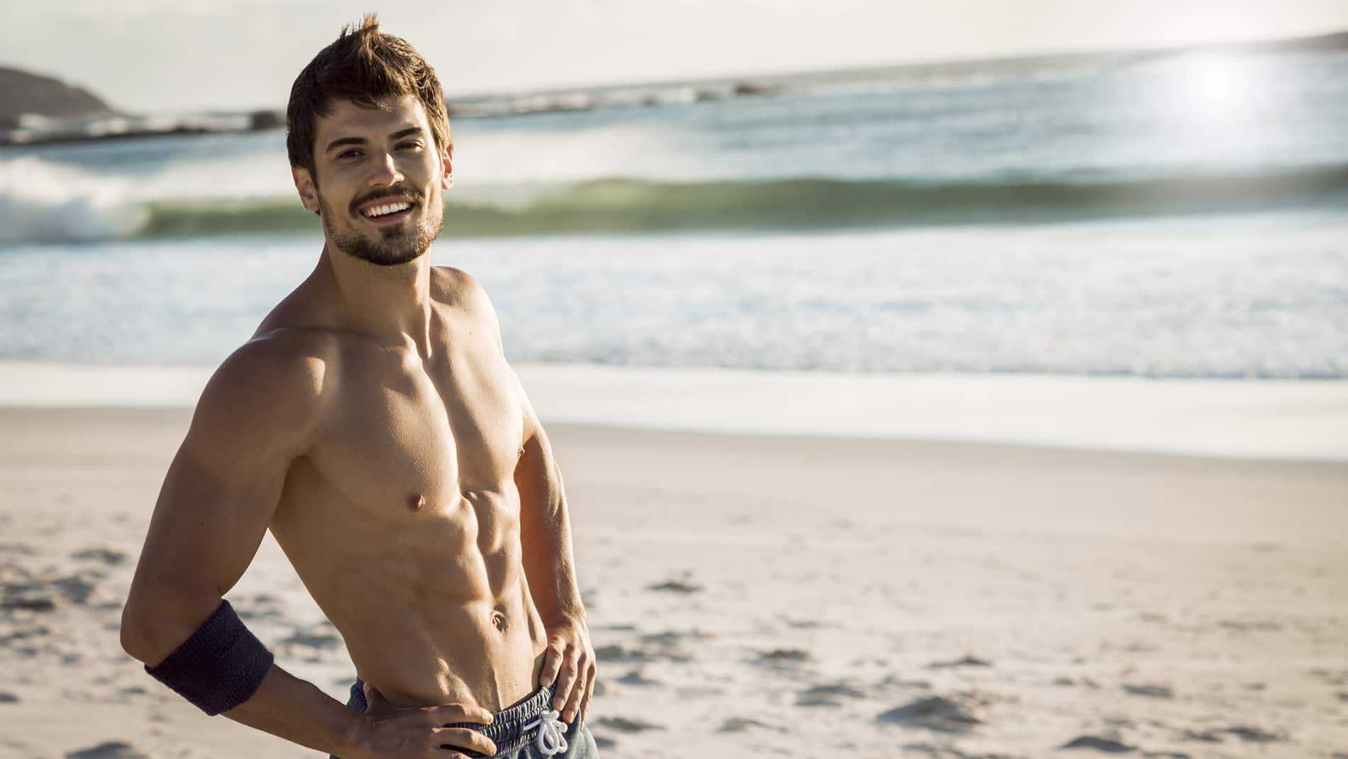 strong fit man smiling and taking a break after hard workout,beautiful weather,sunny day,in the background waves splashing on the beach