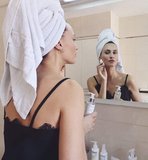 Lima Ché kijkt in de spiegel en heeft skincare verzorgingsproduct in haar hand