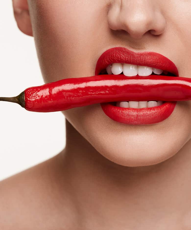 Vrouwelijk gezicht met rode lipstick bijt op een chilipeper