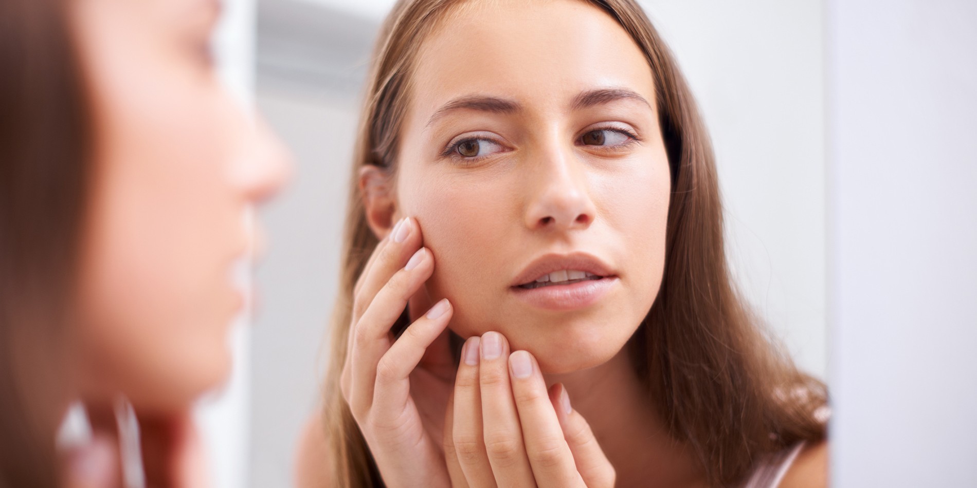 A young woman examining her face in the mirror
