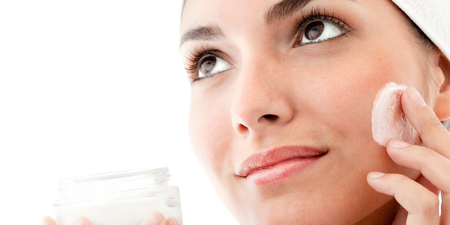 Attractive young woman applies facial cream from a jar. Isolated on white.