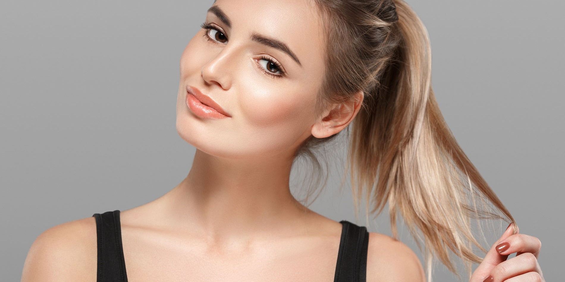 Beautiful young woman portrait smiling posing attractive blond with flying hair on gray background. Studio shot.