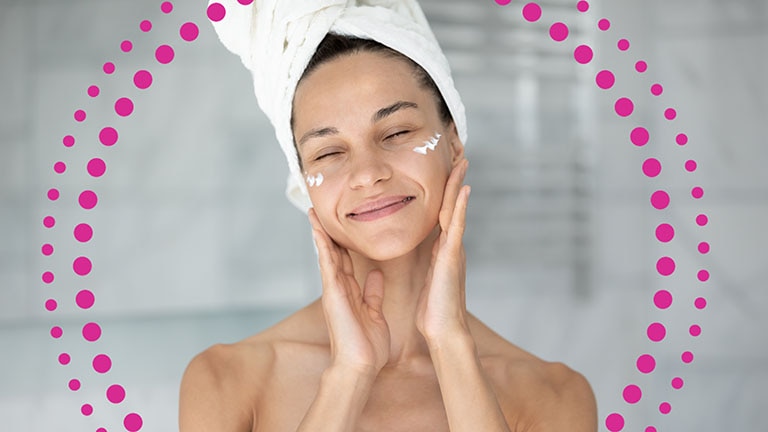  Femme souriante appliquant une crème hydratante sur son visage						 Femme souriante appliquant une crème hydratante sur son visage