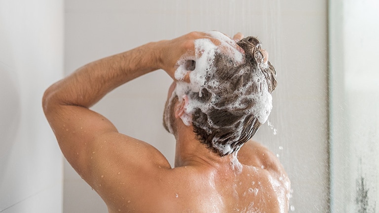 Man wast zijn haren met schuimende shampoo onder de douche. Man wast zijn haren met schuimende shampoo onder de douche.